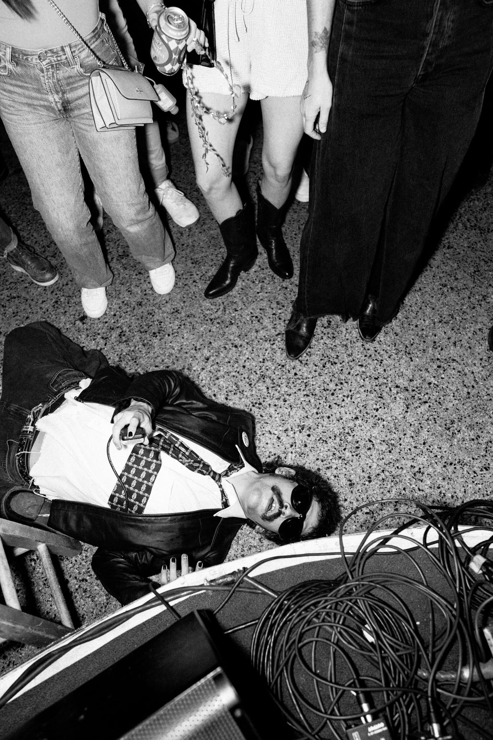 Almost Heaven performing on the floor amid the crowd, the artist in a leather jacket and sunglasses lying back among the audience at C-Boy’s Heart & Soul, Austin TX, black-and-white — live music photographer Chauncey Scott
