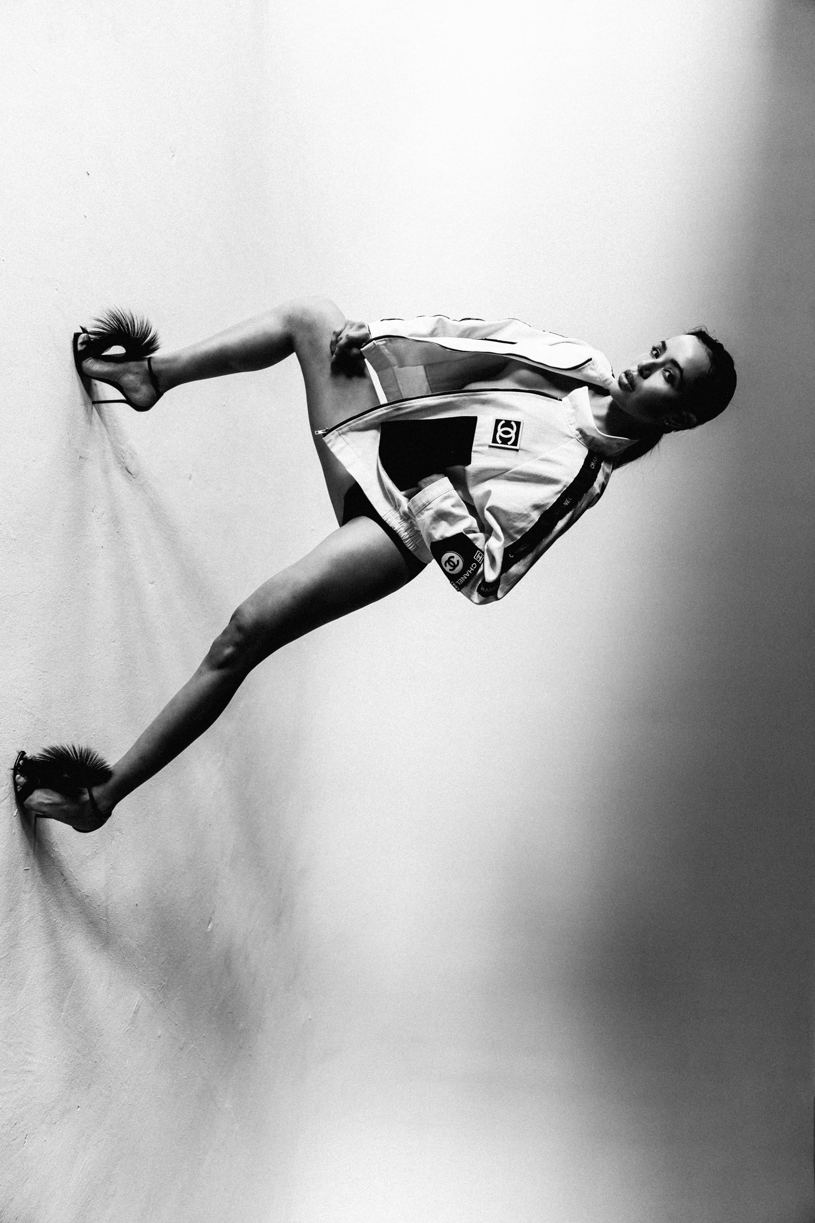Aly Zuniga in an athletic pose with feather-trim heels braced against a studio wall, black-and-white Chanel fashion editorial by Chauncey Scott, Austin TX