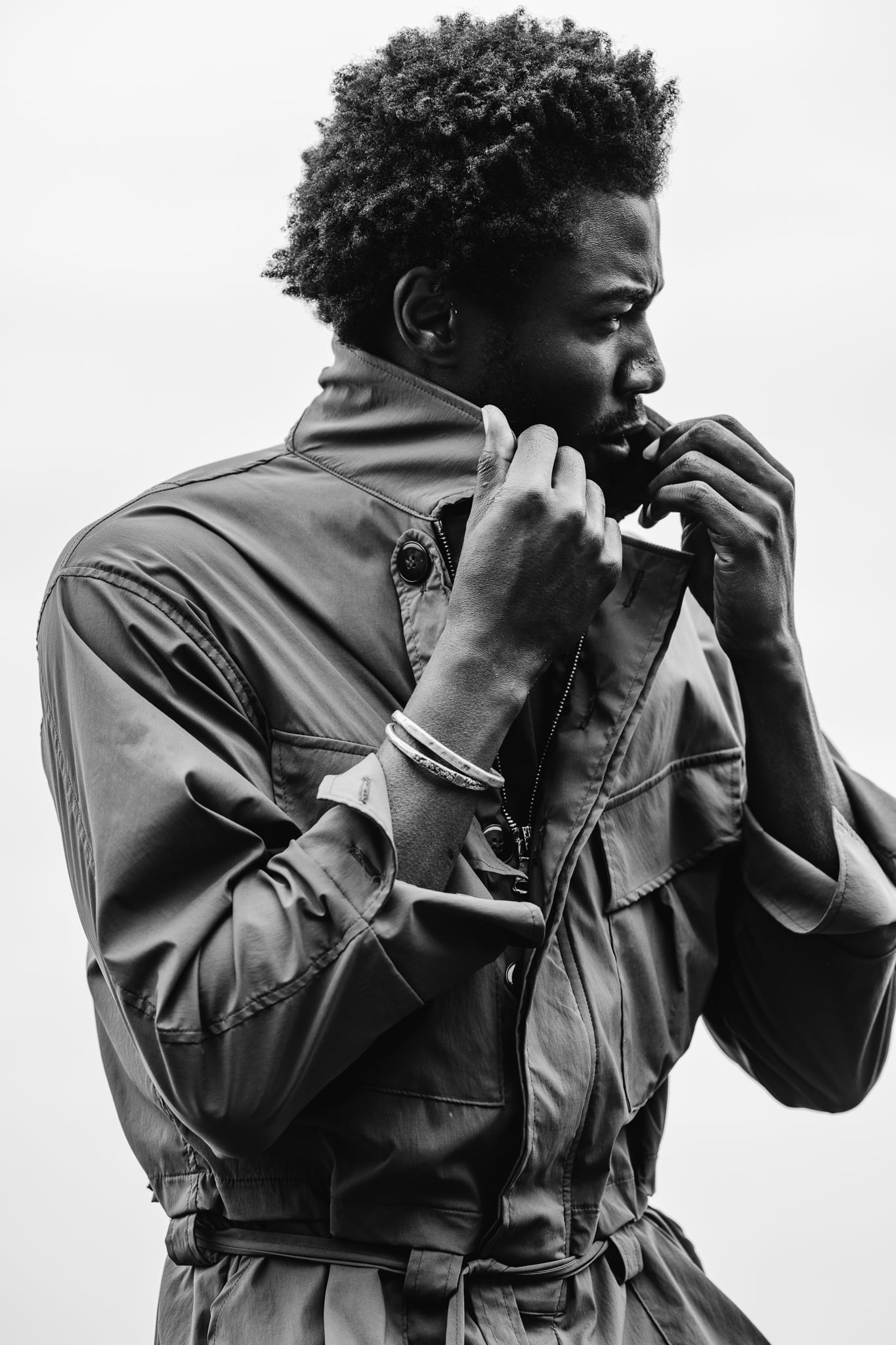 Copala model zipping the collar of an olive utility jacket against the sky, black-and-white menswear lifestyle editorial by Chauncey Scott, Malibu CA