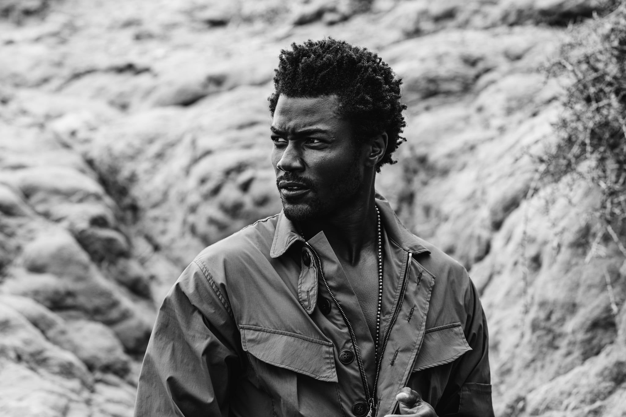 Copala model in an olive coverall and silver chain against a rocky cliff, black-and-white menswear editorial by Chauncey Scott, Leo Carrillo State Beach