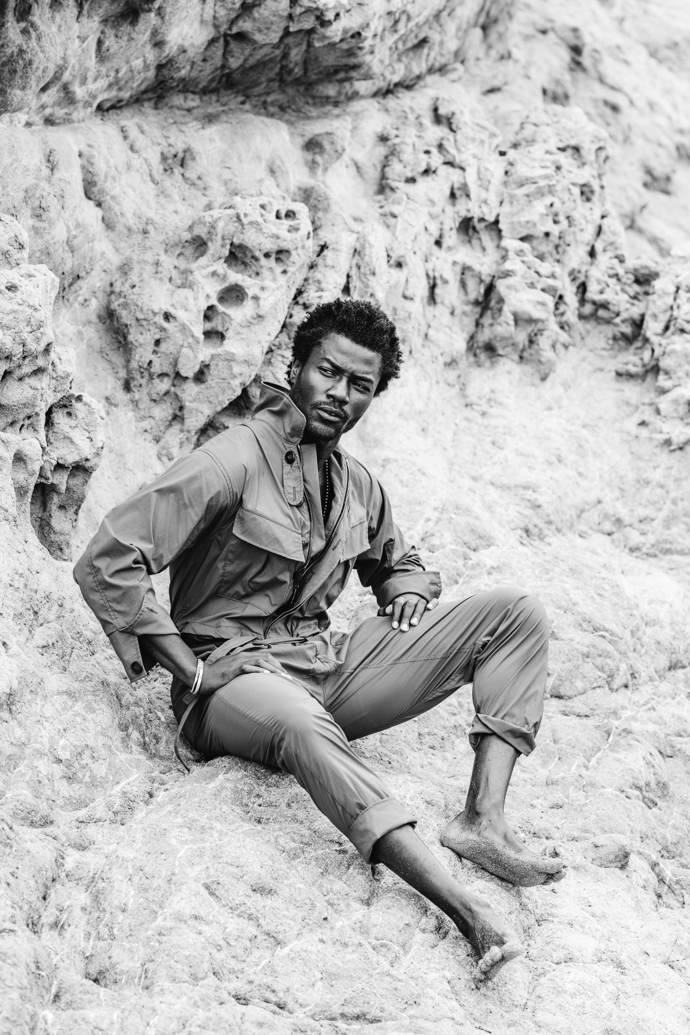 Copala model reclining on pale sandstone in an olive coverall, black-and-white menswear editorial by Chauncey Scott, Leo Carrillo State Beach, Malibu