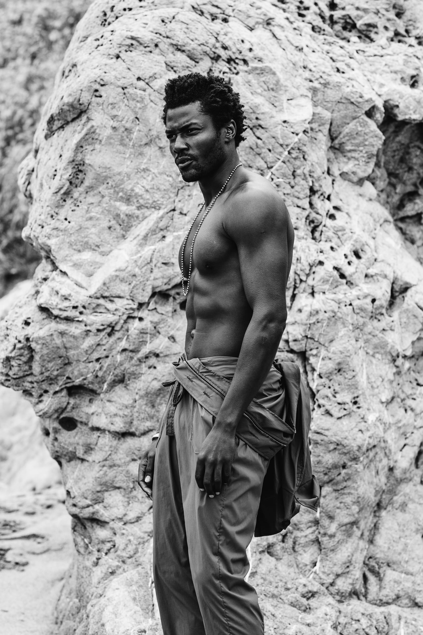 Copala torso detail, shirtless in olive cargo pants with a jacket knotted at the waist and silver bead chain, black-and-white menswear detail by Chauncey Scott, Malibu CA