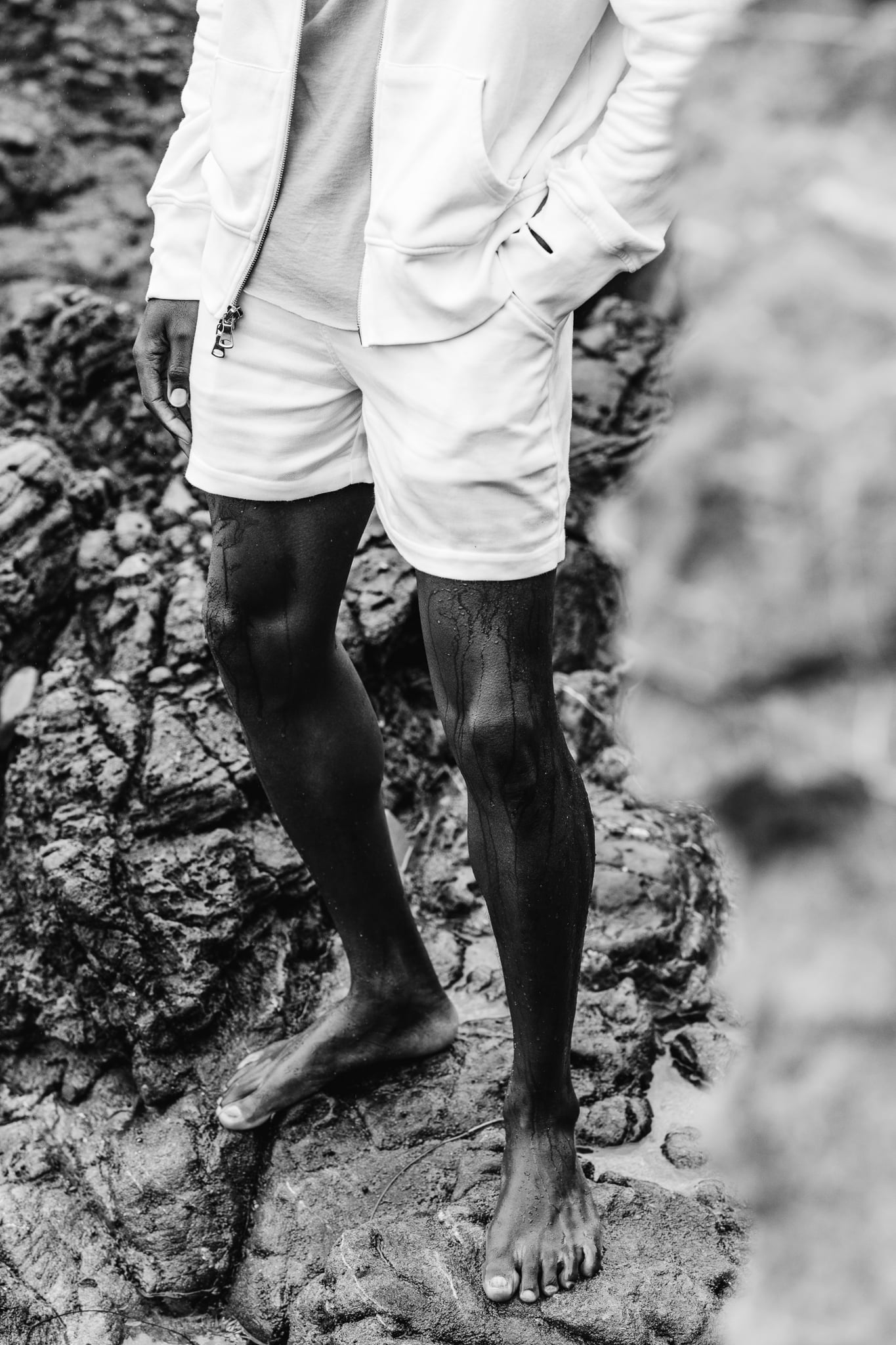 Copala white hoodie and shorts on wet legs standing on coastal rock, black-and-white menswear lifestyle editorial by Chauncey Scott, Leo Carrillo State Beach