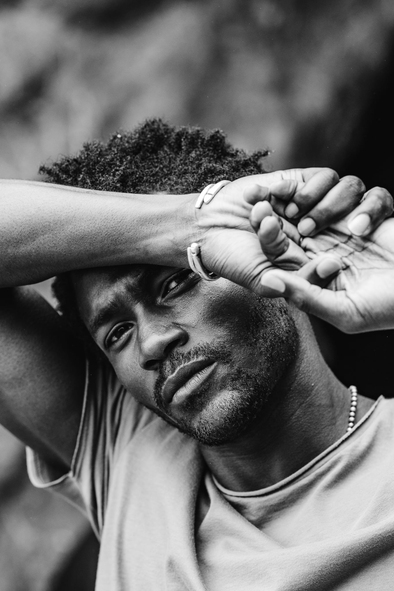 Copala model lying back with wrists crossed over his forehead in a taupe tee and silver chain, black-and-white menswear portrait by Chauncey Scott, Malibu CA