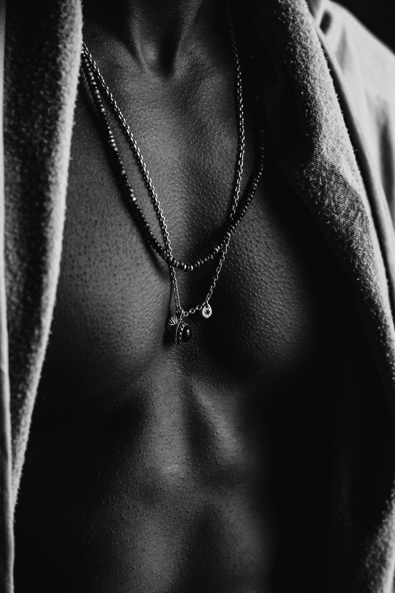 Close-up of layered silver bead and chain necklaces on the Copala model's bare chest, black-and-white menswear jewelry detail by Chauncey Scott, Malibu CA