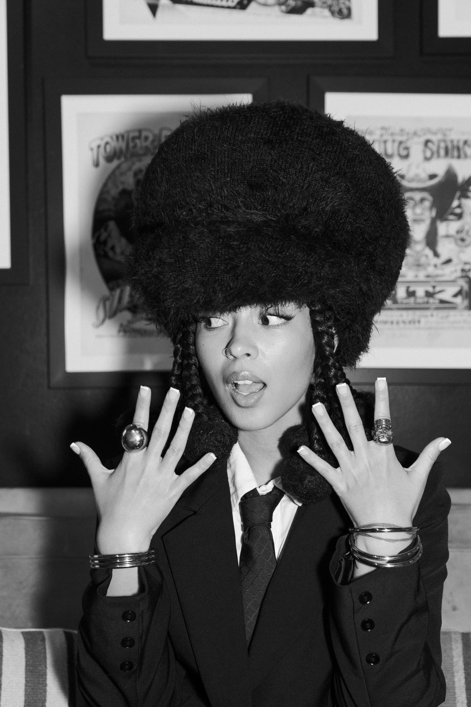 Dizzy Fae, black-and-white close-up editorial portrait in a tall fur hat, suit and skinny tie, against framed vintage gig posters, Waterloo Records, Austin TX — editorial portrait photography by Chauncey Scott