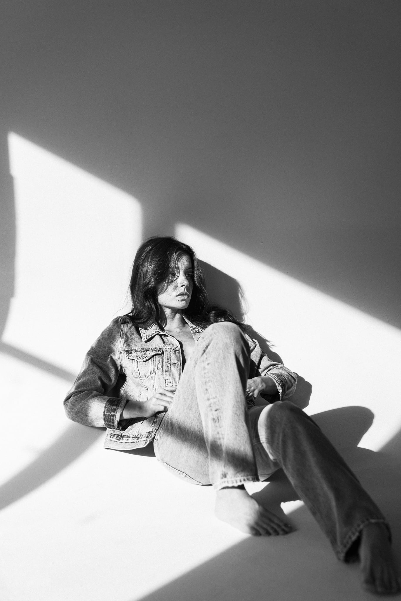Lillian Connell seated on the floor in a Levi's denim jacket and jeans as window light cuts across the wall, black-and-white studio portrait by Chauncey Scott, Austin TX