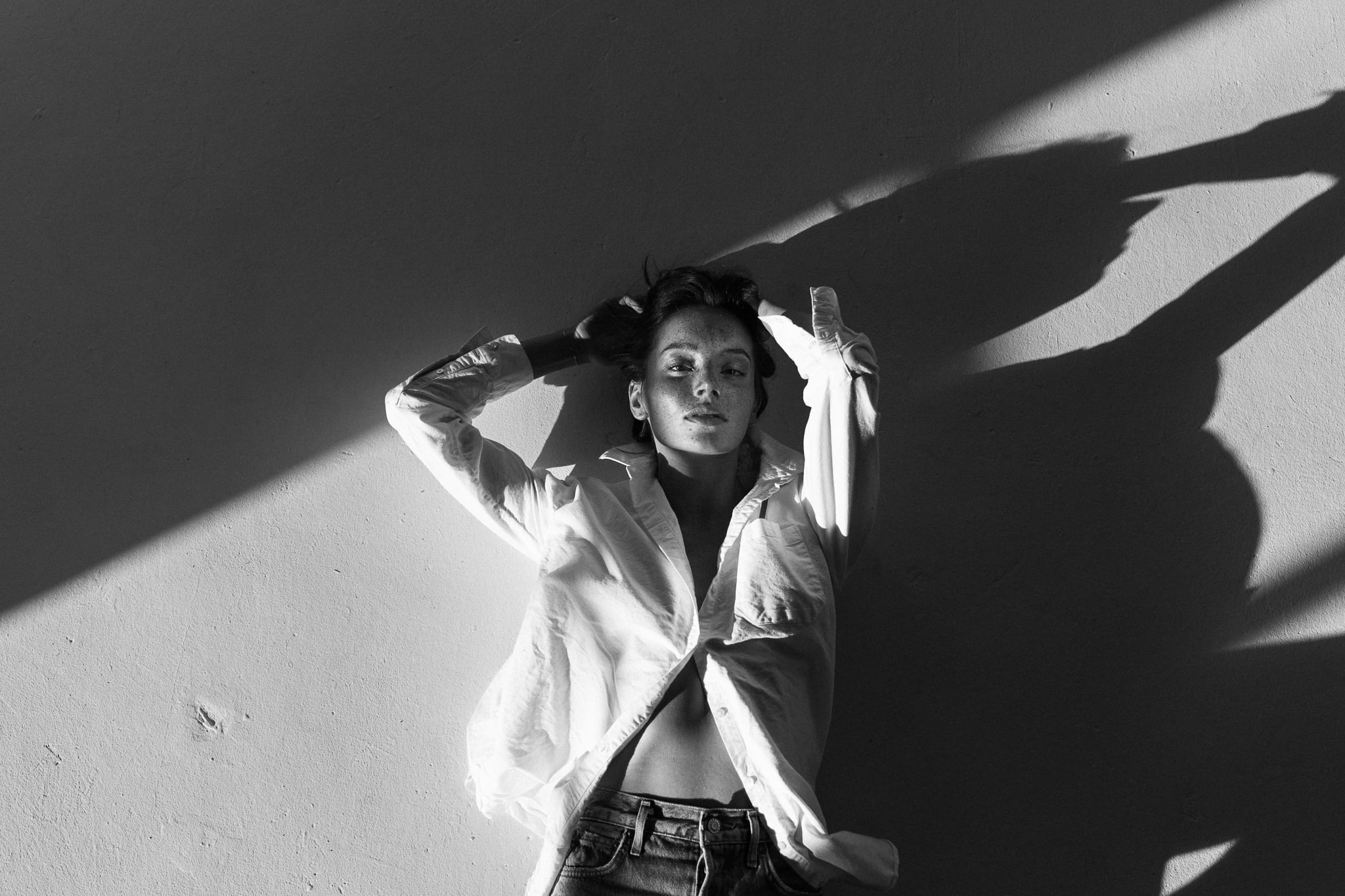 Lillian Connell against a wall in an open white shirt as her arms cast dramatic shadows, black-and-white studio editorial by Chauncey Scott, Austin TX