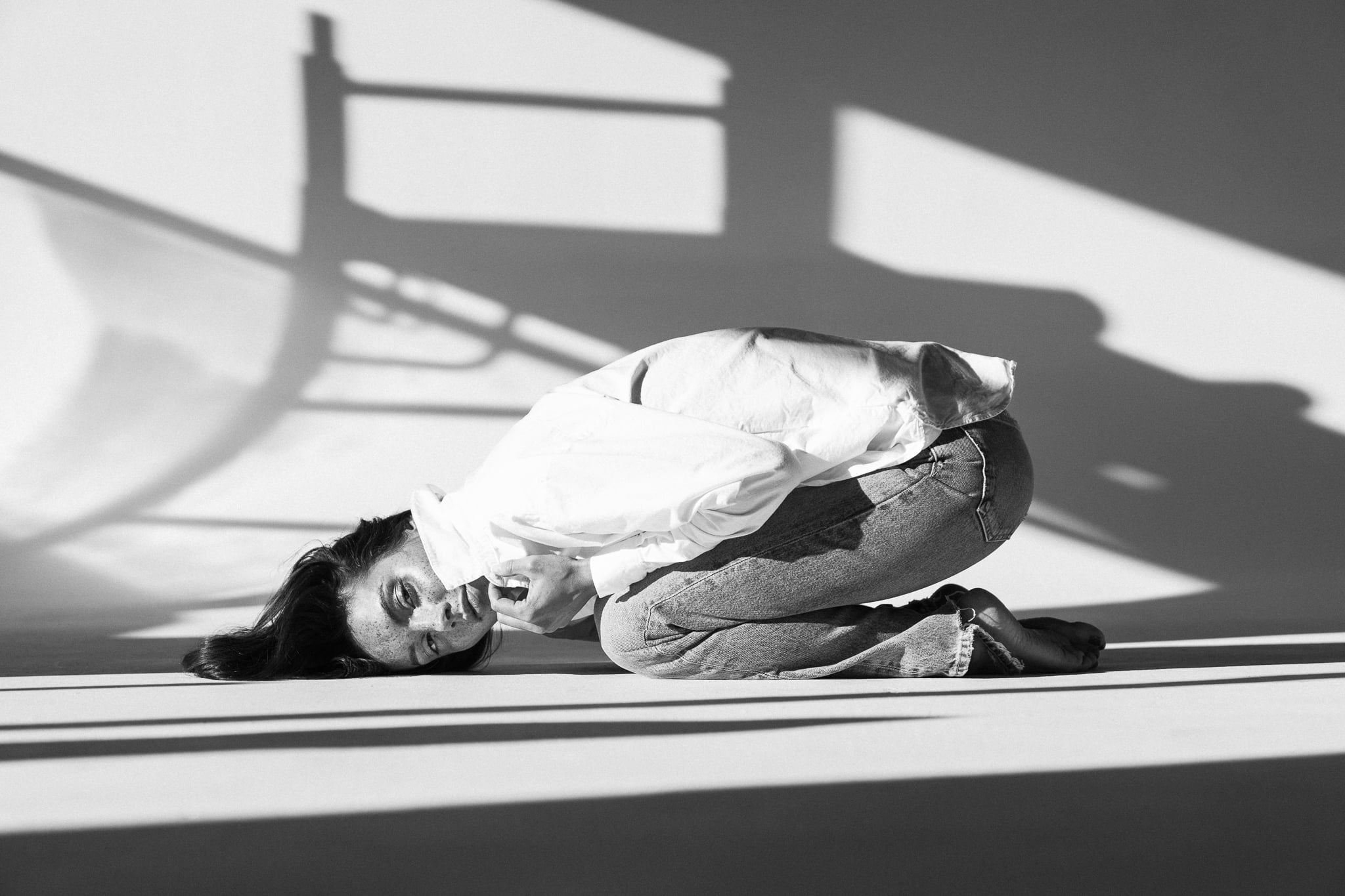 Lillian Connell lying on the floor in a white shirt and jeans under hard window light, black-and-white studio editorial by Chauncey Scott, Austin TX