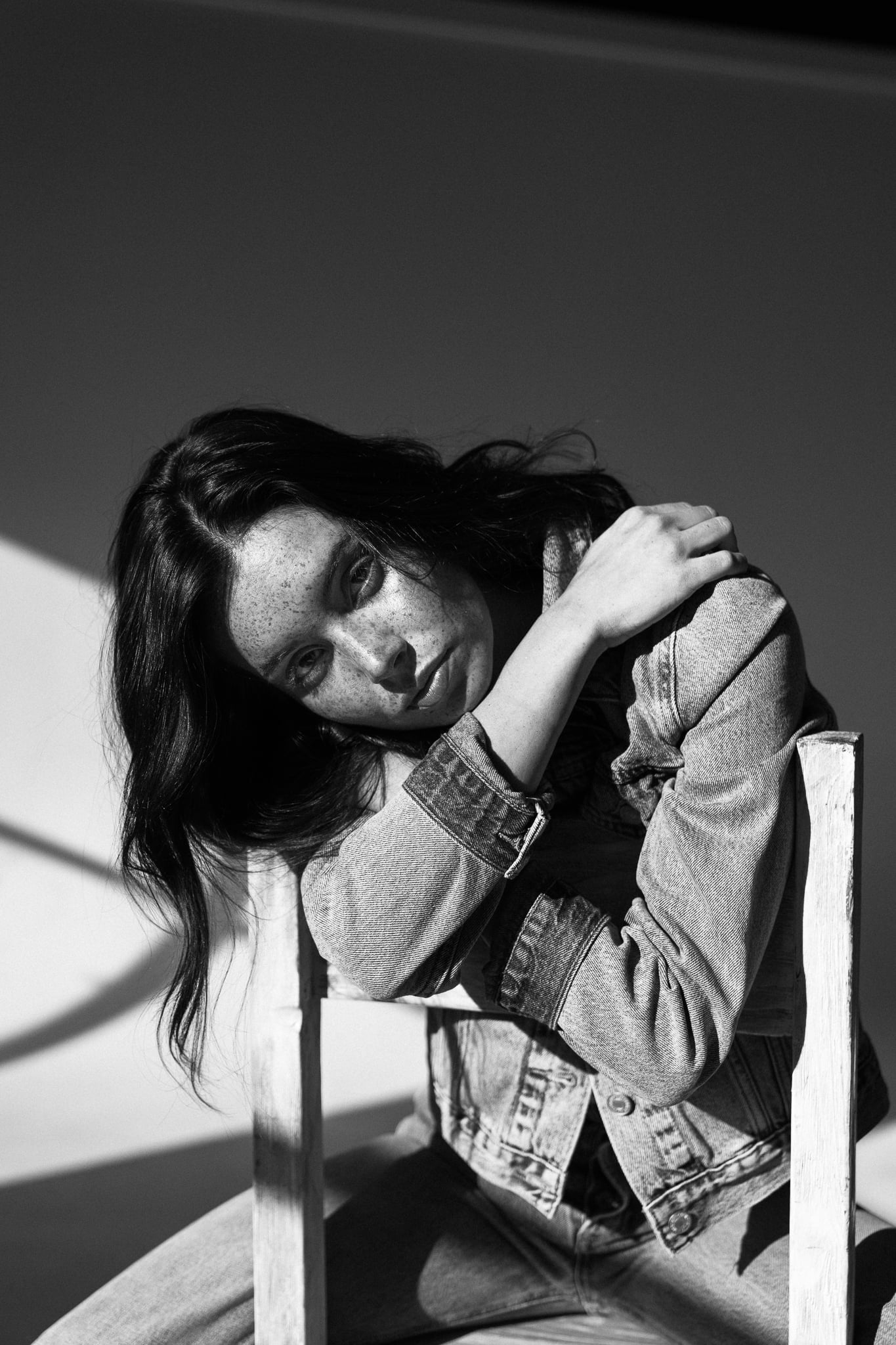 Lillian Connell resting her head on a wooden chair back in a Levi's denim jacket, freckled black-and-white portrait by Chauncey Scott, Austin TX