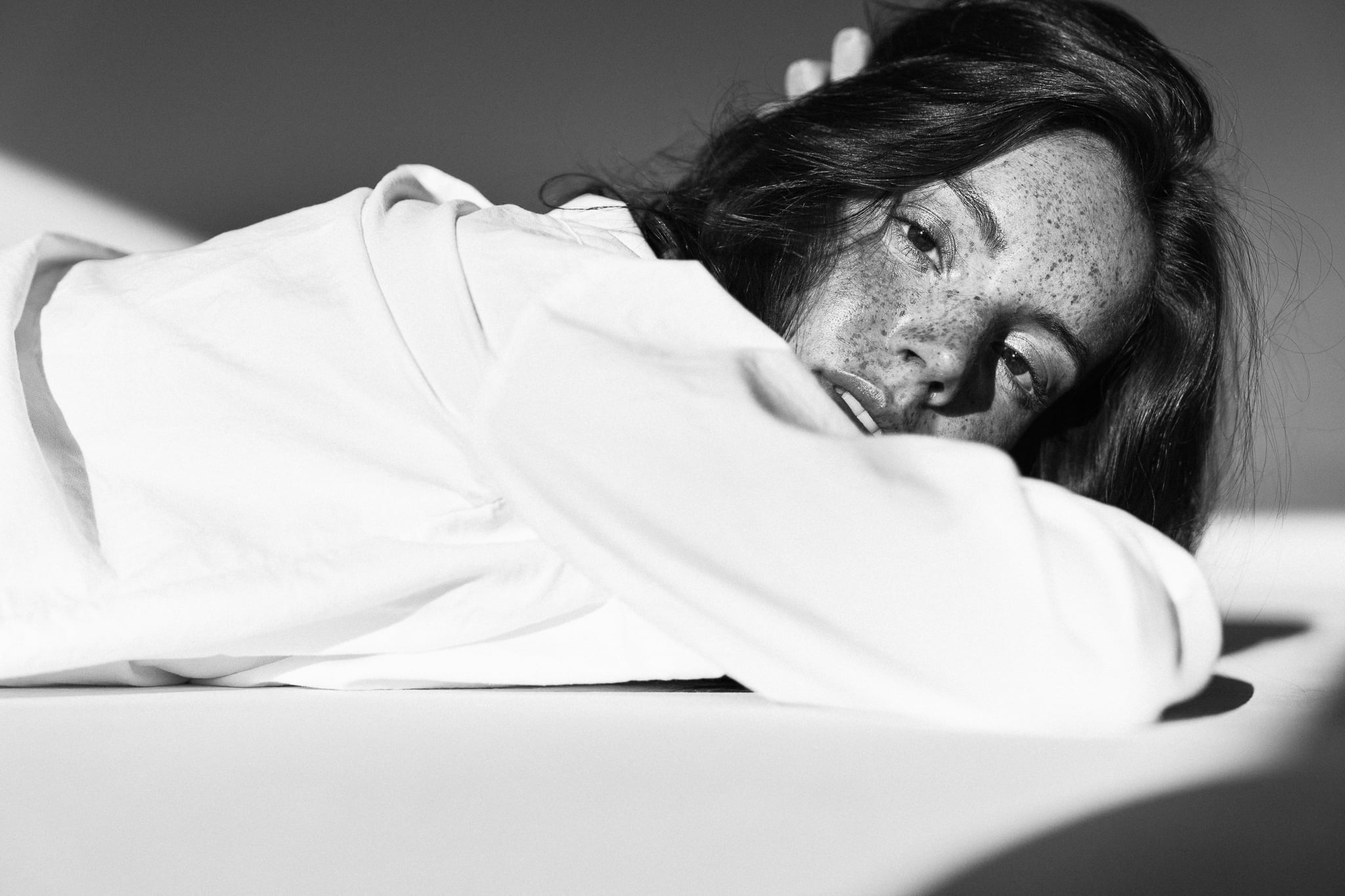 Lillian Connell lying on her side with her face on her arm in a white shirt, freckled black-and-white portrait by Chauncey Scott, Austin TX