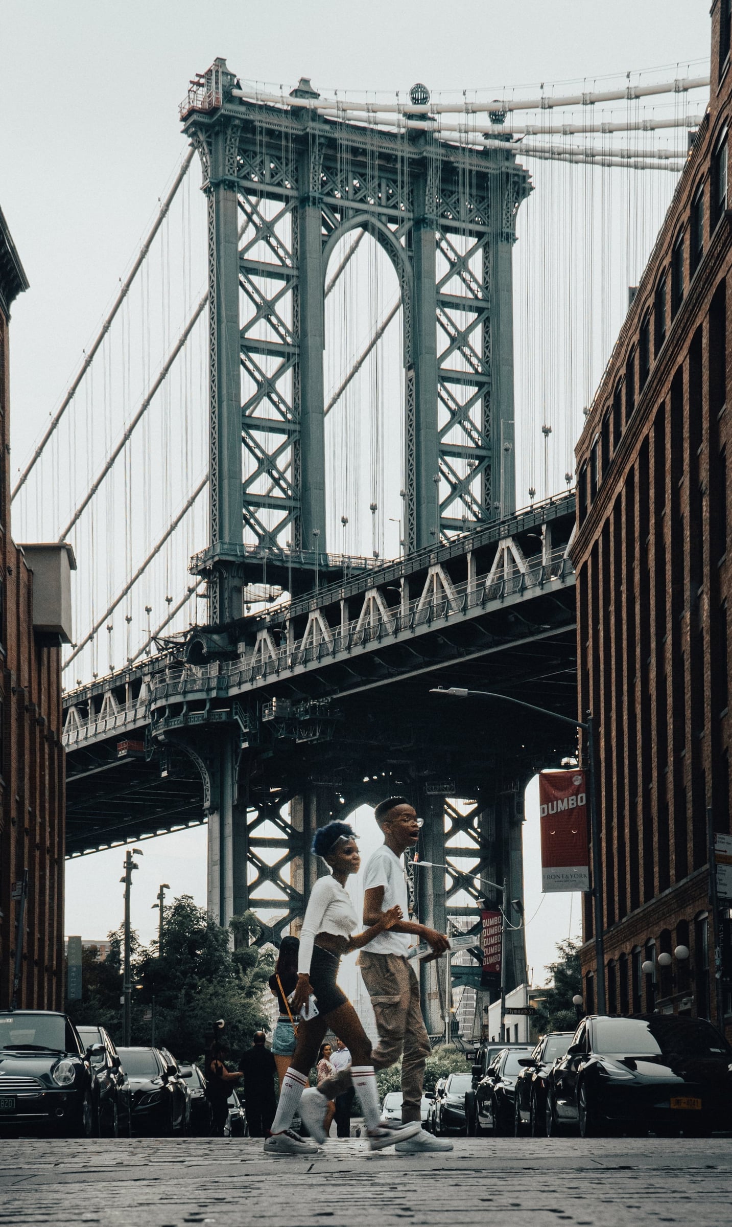 Two people walking in DUMBO, Brooklyn, New York City with Manhattan Bridge in background — editorial street photography by Chauncey Scott, commercial photographer