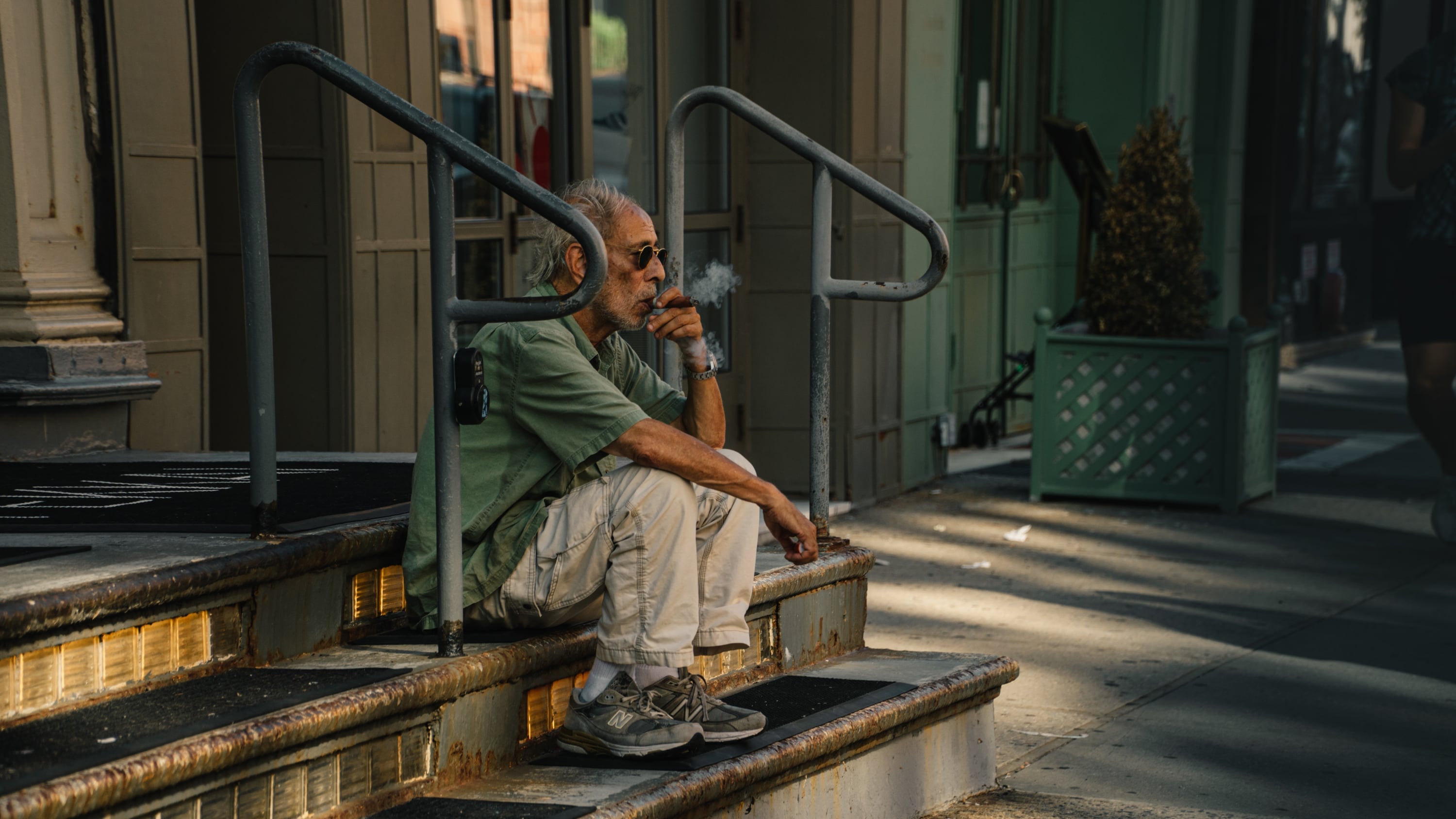 Older man smoking on the cast-iron storefront steps of a SoHo building, Manhattan, New York City — editorial street and documentary photography by Chauncey Scott