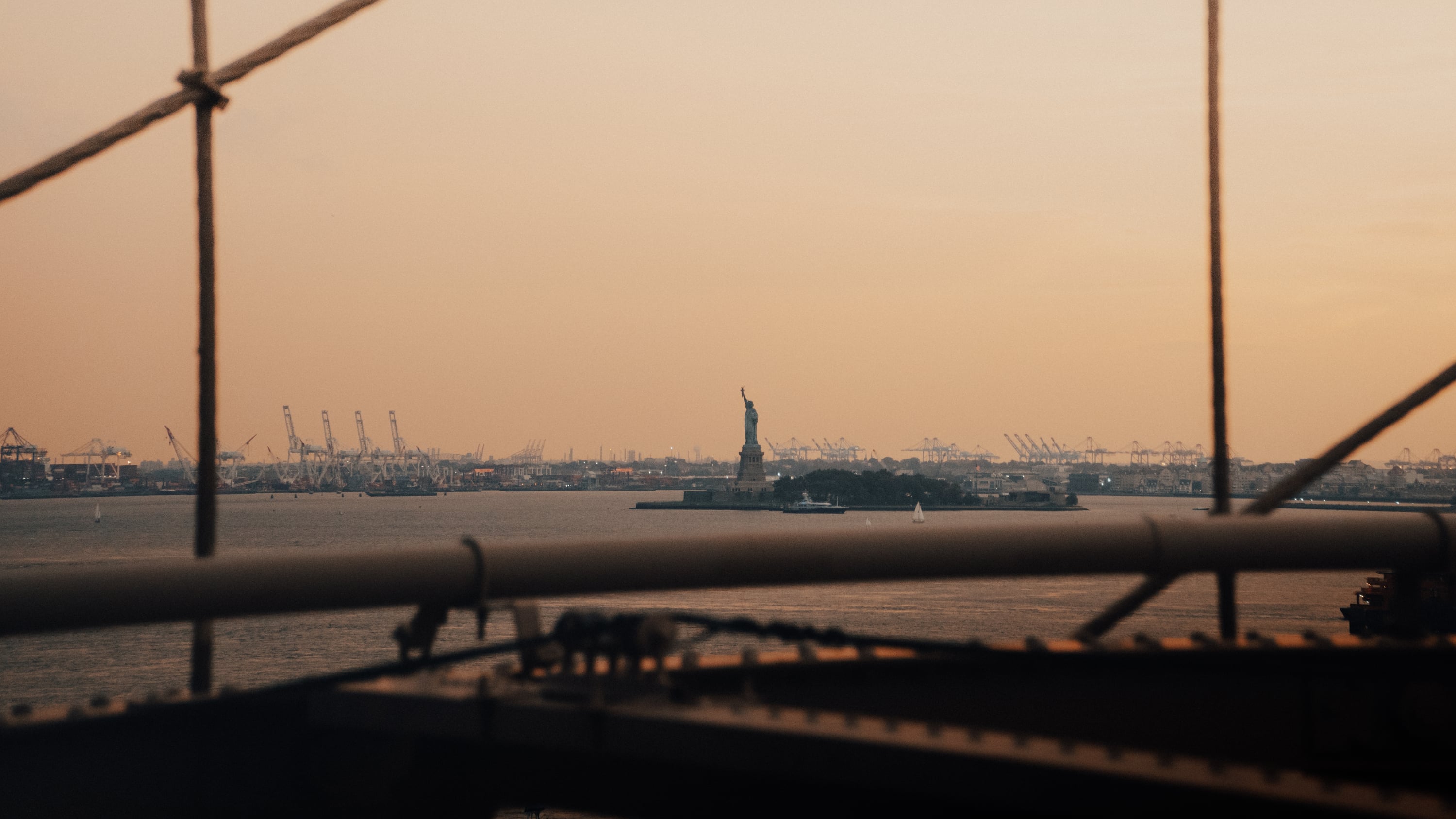 Statue of Liberty and New York Harbor at sunset framed through Brooklyn Bridge cables, New York City — editorial photography by Chauncey Scott