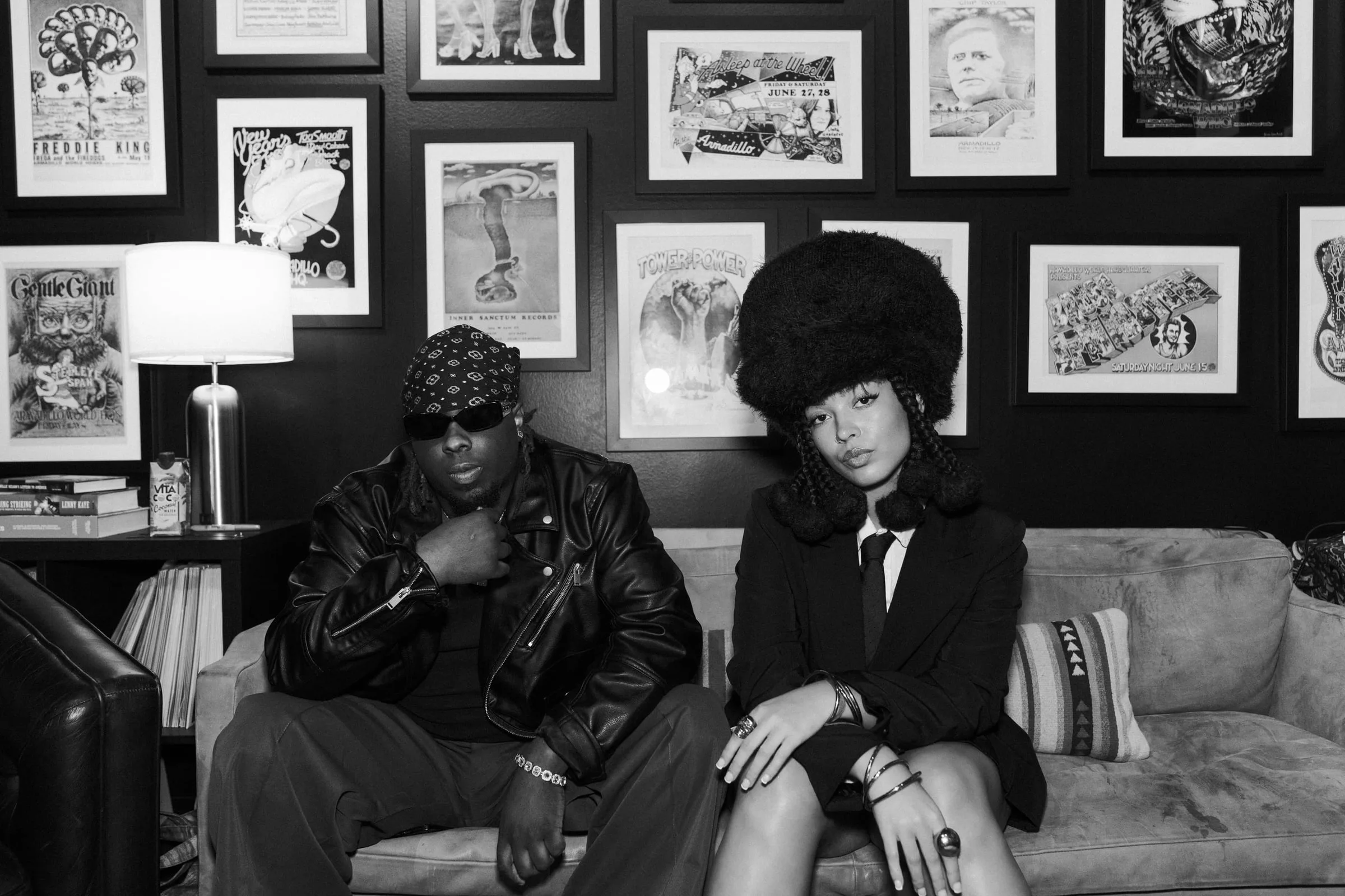 Dizzy Fae and Blk Odyssey, black-and-white editorial portrait on a velvet couch beneath framed vintage gig posters, Waterloo Records, Austin TX — editorial music photography by Chauncey Scott